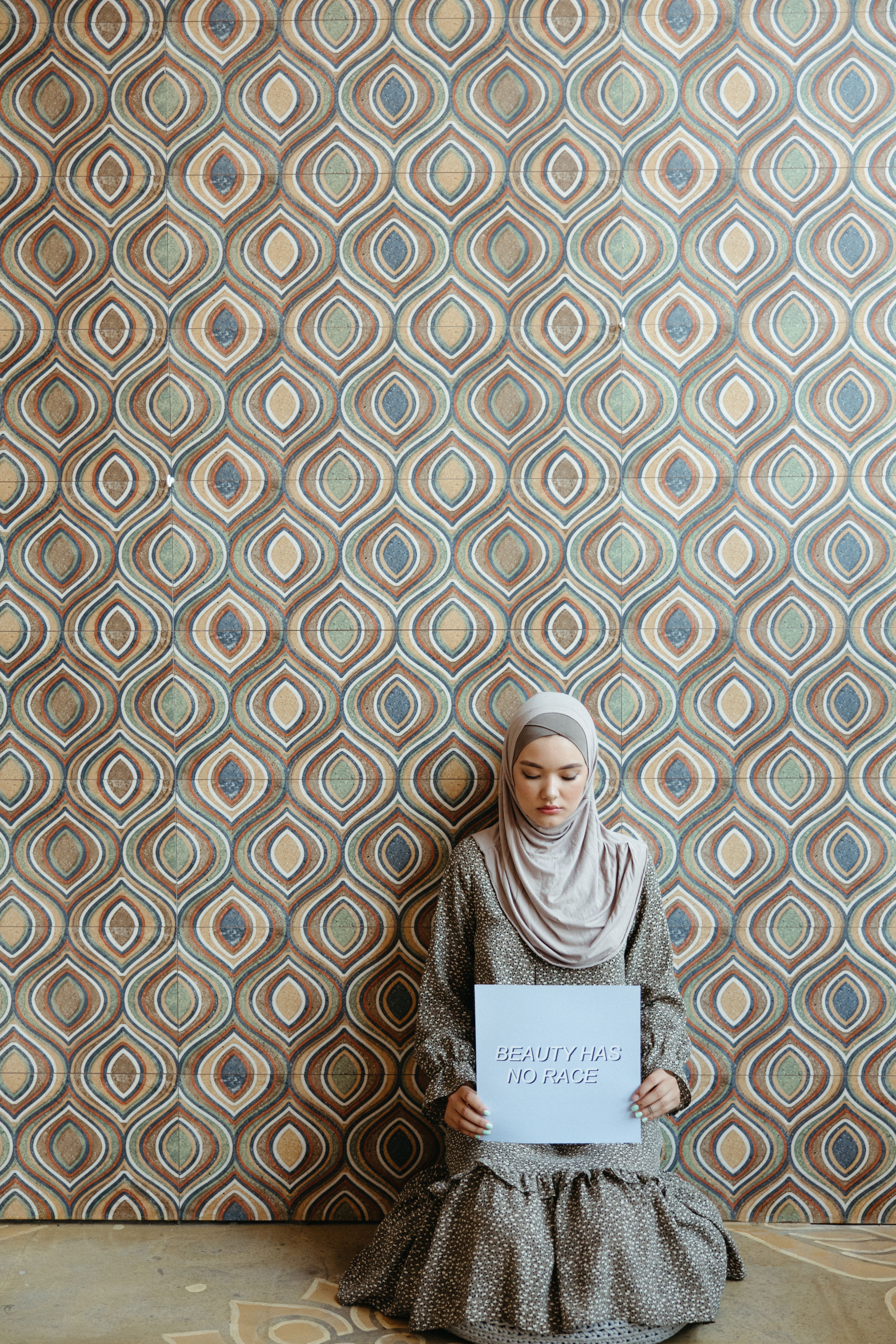 Young Muslim woman in hijab holding a poster with a patterned background.