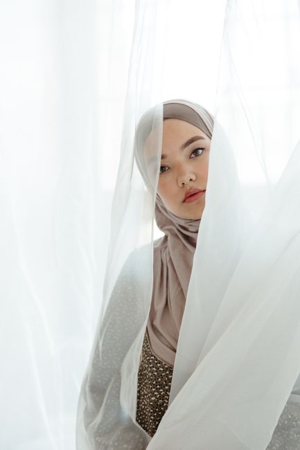 Graceful portrait of a young woman in a hijab behind sheer curtains, capturing beauty and elegance.