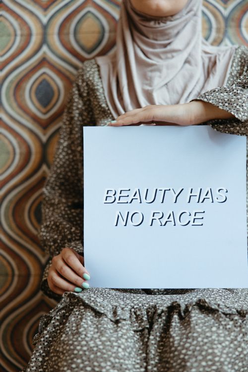 Free Close-up of a woman in a hijab holding a sign with the slogan 'Beauty Has No Race,' promoting diversity and empowerment. Stock Photo