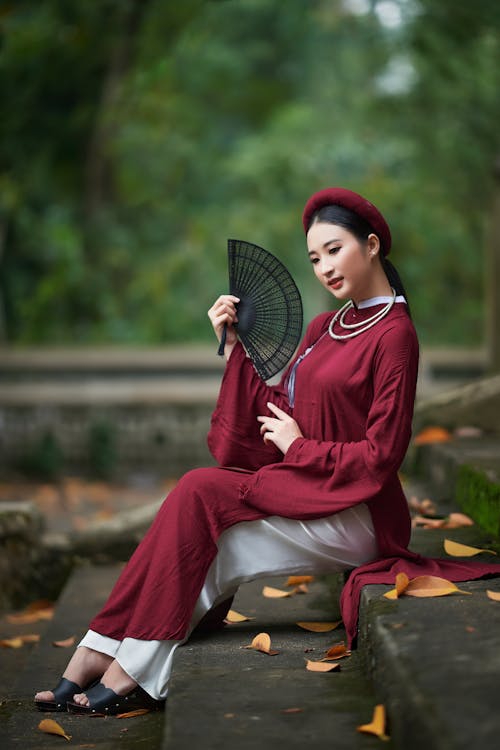 Woman in Traditional Clothing Holding a Fan Sitting on Steps 