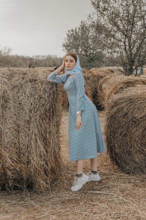 Woman in Blue Dress Standing Beside Haystacks