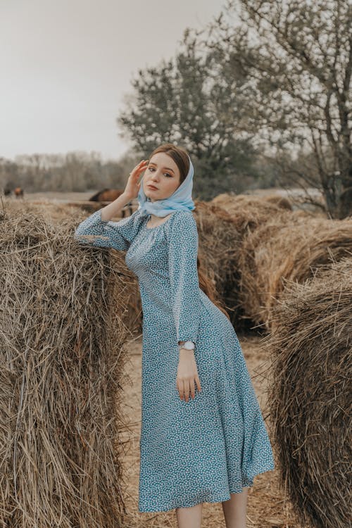 Woman in Blue Dress Standing Between Haystacks
