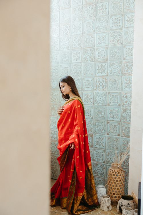 Free Portrait of a woman in a red and black traditional saree, standing indoors against a decorative wall. Stock Photo