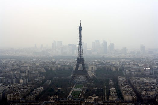 A foggy view of the Eiffel Tower rising above the Paris cityscape, capturing the city's iconic architecture.
