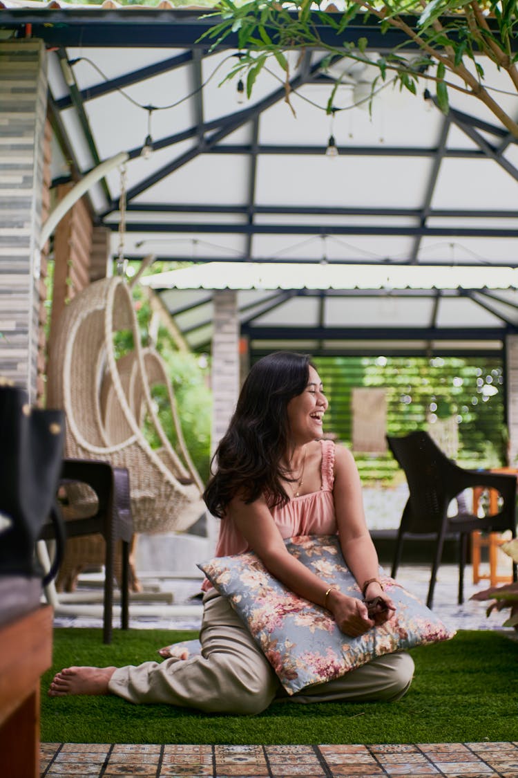 Smiling Woman Sitting On A Patio Holding A Cushion 