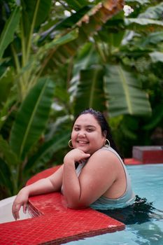 Smiling woman enjoying her time in a tropical pool surrounded by lush greenery.