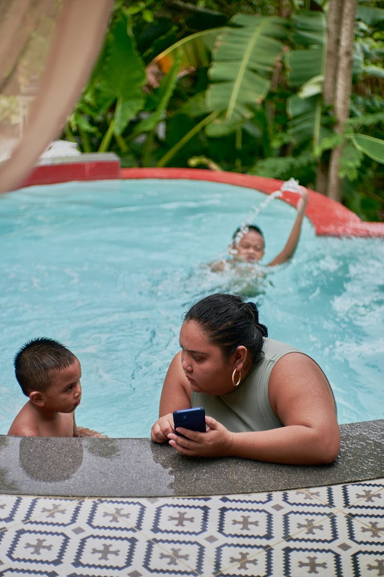 Woman Holding Mobile Phone And Talking To A Child In Pool