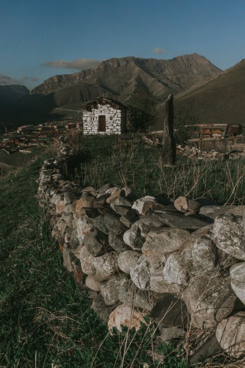 Free Stone hut on a hillside with mountain backdrop in North Ossetia, capturing rural beauty. Stock Photo