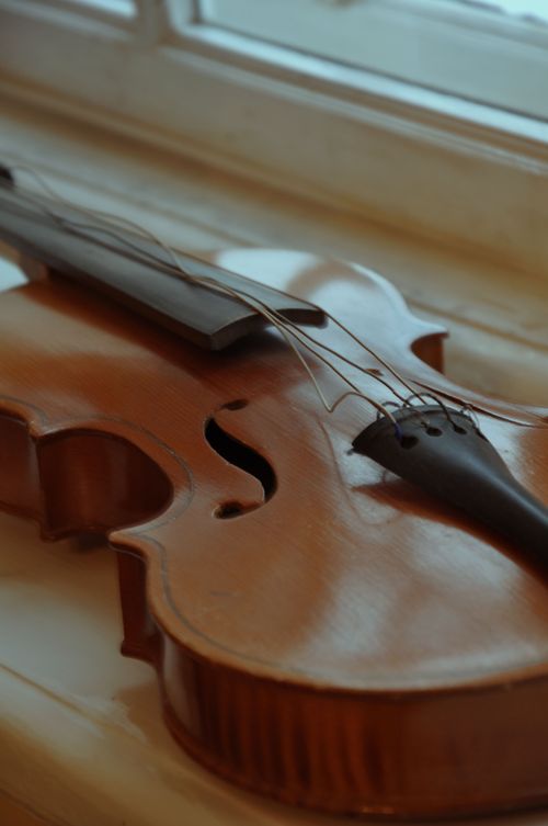 Free A detailed close-up of a vintage violin resting by a window, with a soft warm tone. Stock Photo