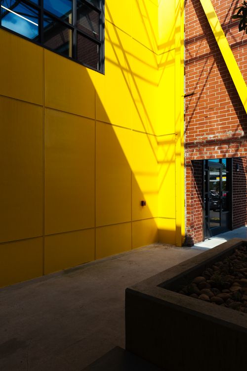 Free Urban architecture with vibrant yellow wall and red brick exterior in sunlight. Stock Photo