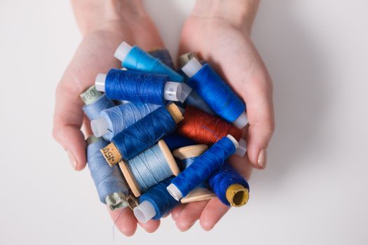 Hands holding colorful sewing threads on a white surface, embodying creativity and craftsmanship.