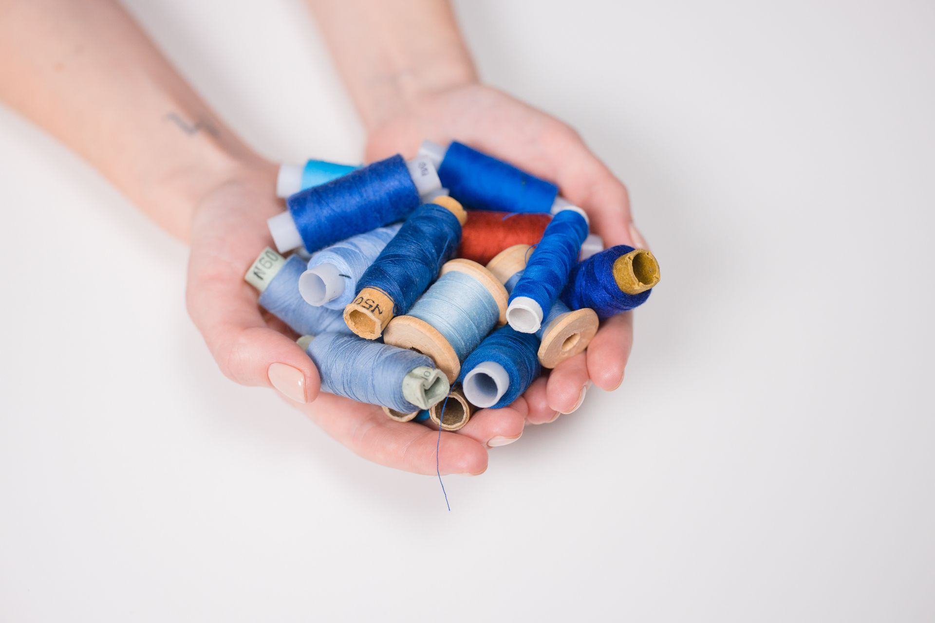 A close-up shot of diverse colorful sewing threads held in hands against a white background.