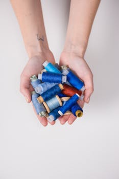 Hands holding various blue sewing threads, highlighting craftsmanship and creativity.