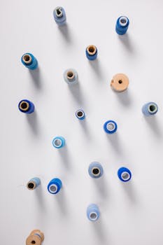 Top view of various blue and beige sewing threads arranged on a white surface.