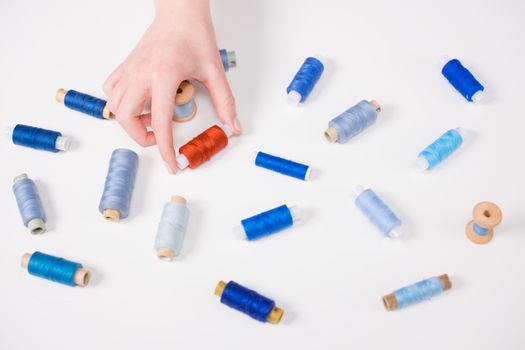 A hand selecting colorful sewing threads on a white surface, showcasing textile art.