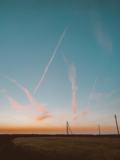 Free Silhouette of utility poles and contrails against a vivid sunset sky over a countryside field. Stock Photo