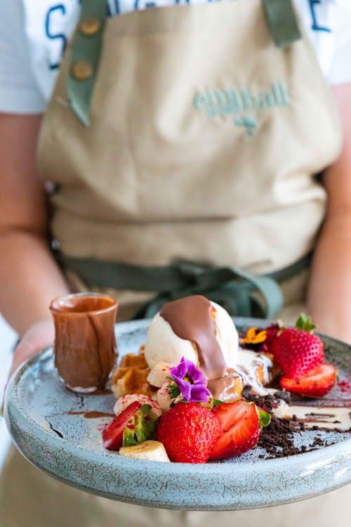 Person Holding Ice Cream with Strawberries and Caramel on Top