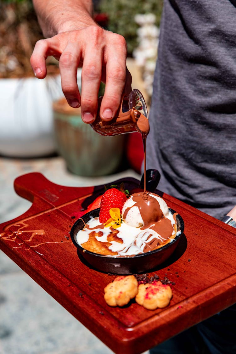 A Person Pouring Melted Chocolate On Ice Cream