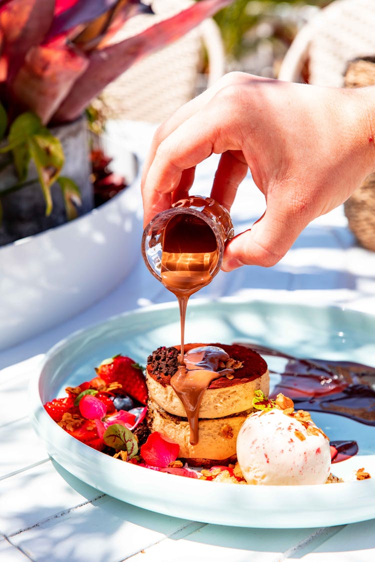 Person Pouring Chocolate On A Dessert Cake 