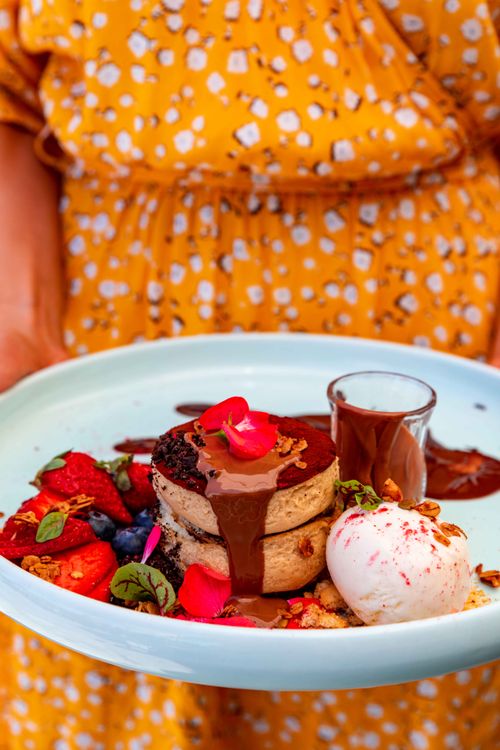 Free Close-up of layered pancakes drizzled with chocolate, paired with fruits and ice cream on a plate. Stock Photo