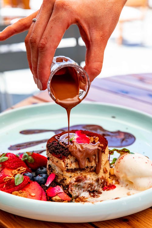 A Person Pouring Melted Chocolate on a Dessert 