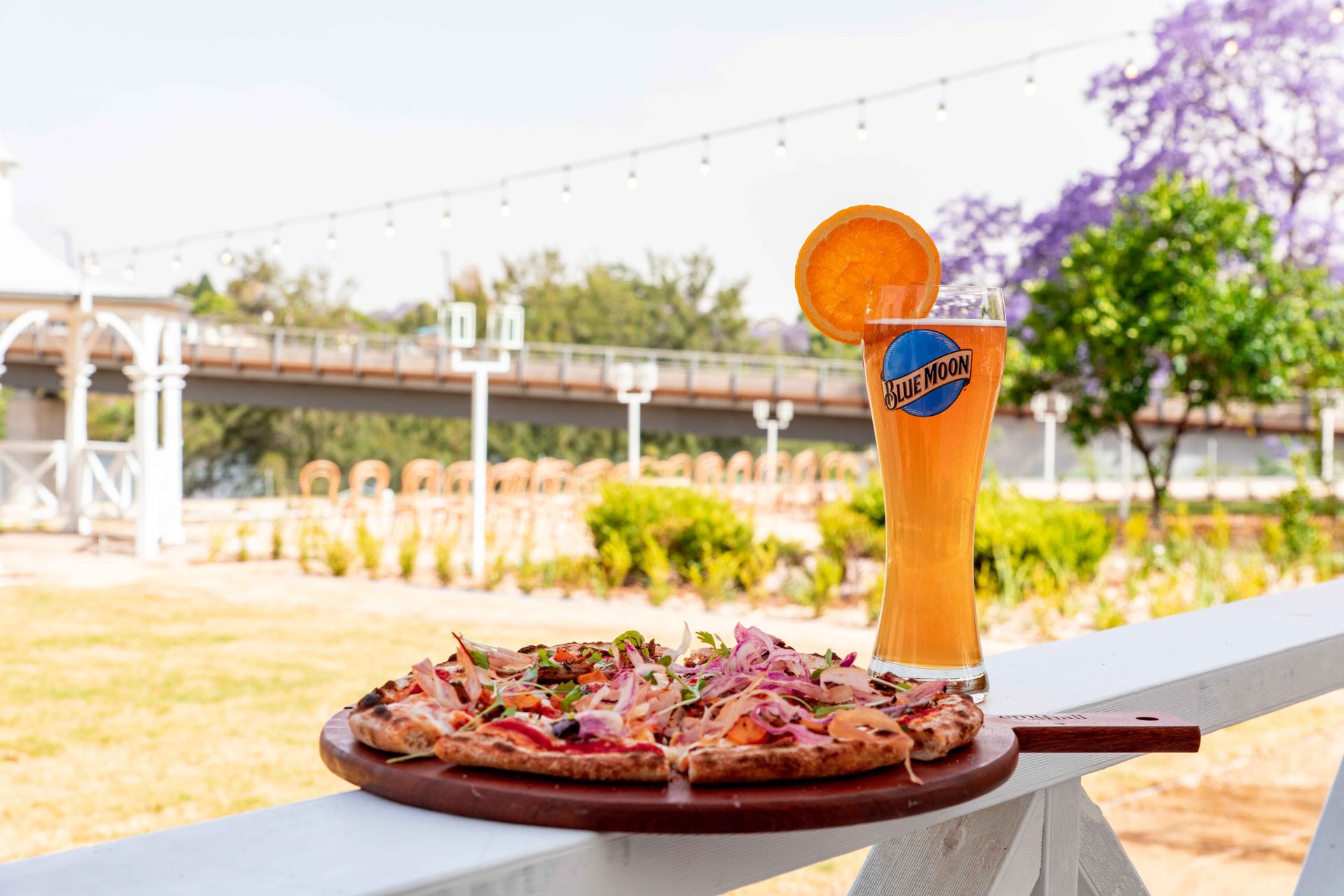 Indulge in an outdoor dining experience with delicious pizza and a refreshing craft beer in a scenic setting.