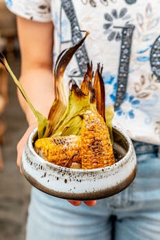 Close-up of grilled corn served in a rustic ceramic bowl, held by a person.