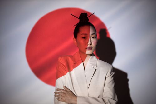 Free An artistic portrait of a woman with a projected Japanese flag background, highlighting cultural themes. Stock Photo