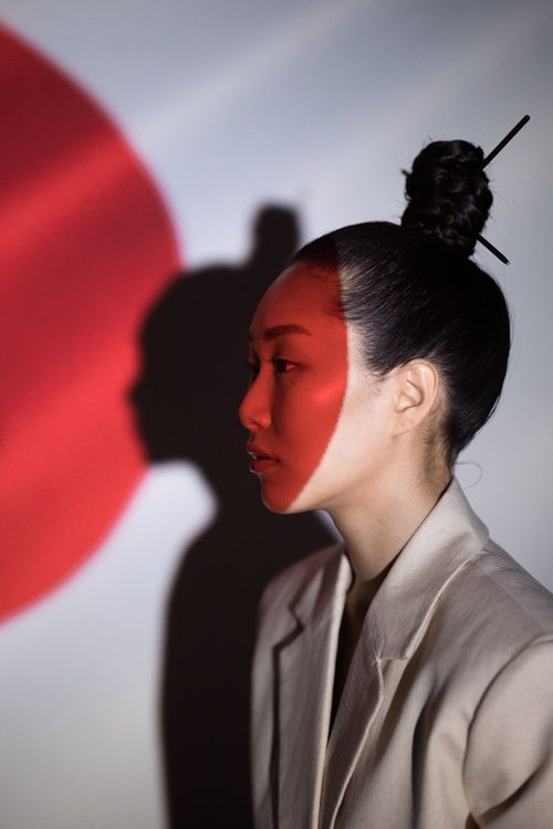 Free Side profile of an Asian woman with a bold red projection resembling the Japanese flag, creating a striking conceptual portrait. Stock Photo