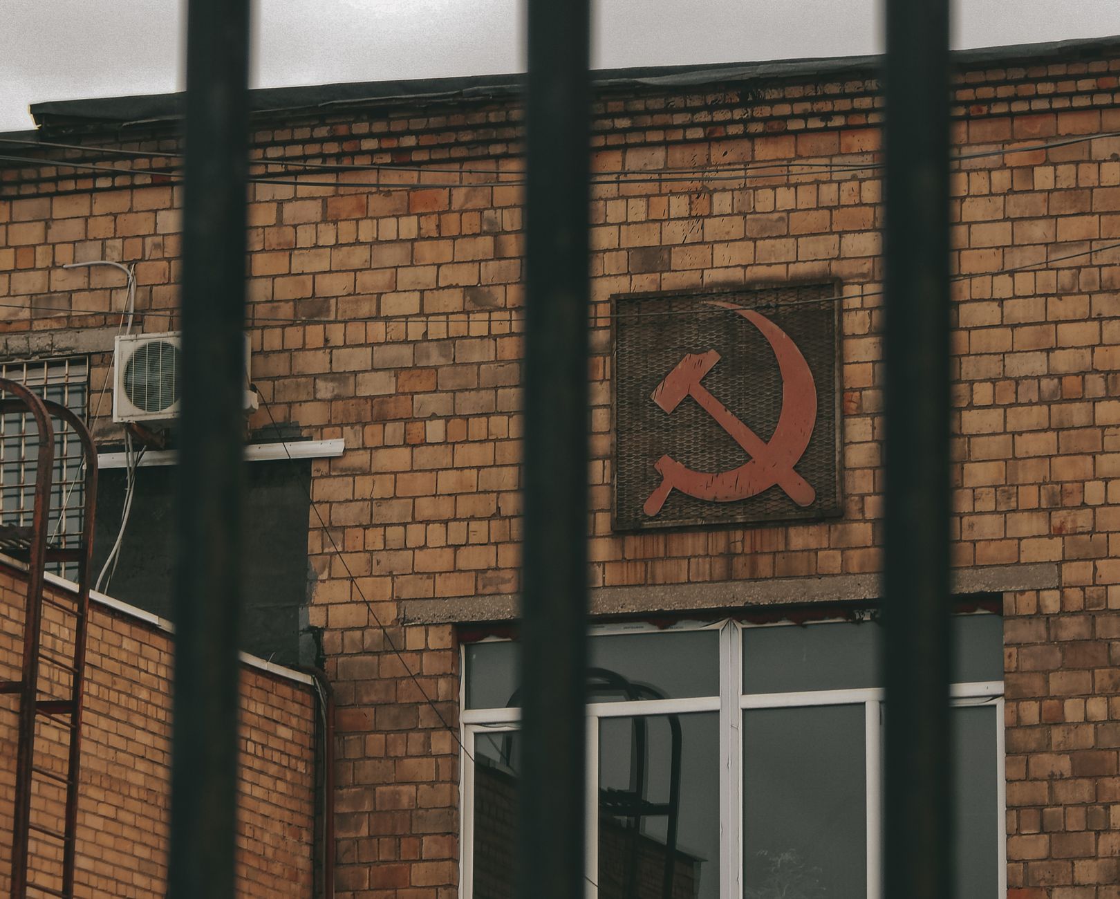 Brick building featuring Soviet hammer and sickle symbol behind metal bars.