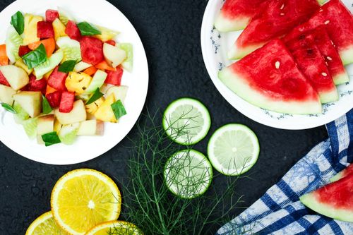 Free Colorful fruit salad and watermelon slices on plates with citrus and greens. Stock Photo