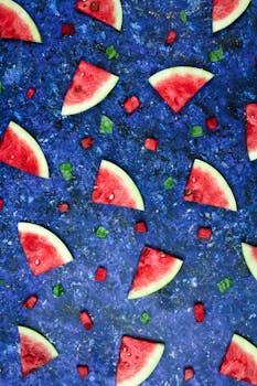 Juicy watermelon slices and cubes on a vibrant blue surface, arranged in an artistic pattern.