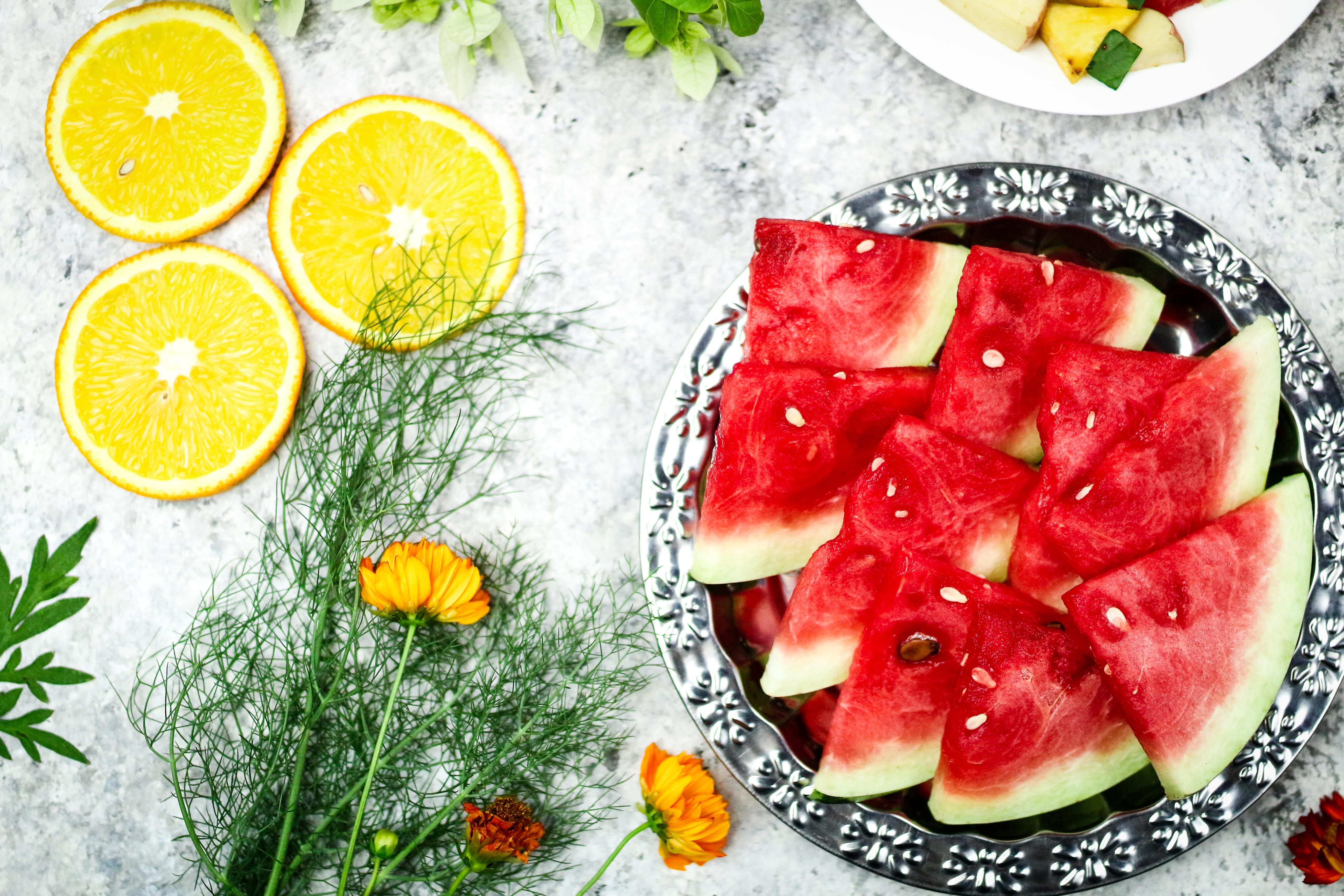 Vibrant sliced watermelon and orange fruits on a table with herbs and flowers.