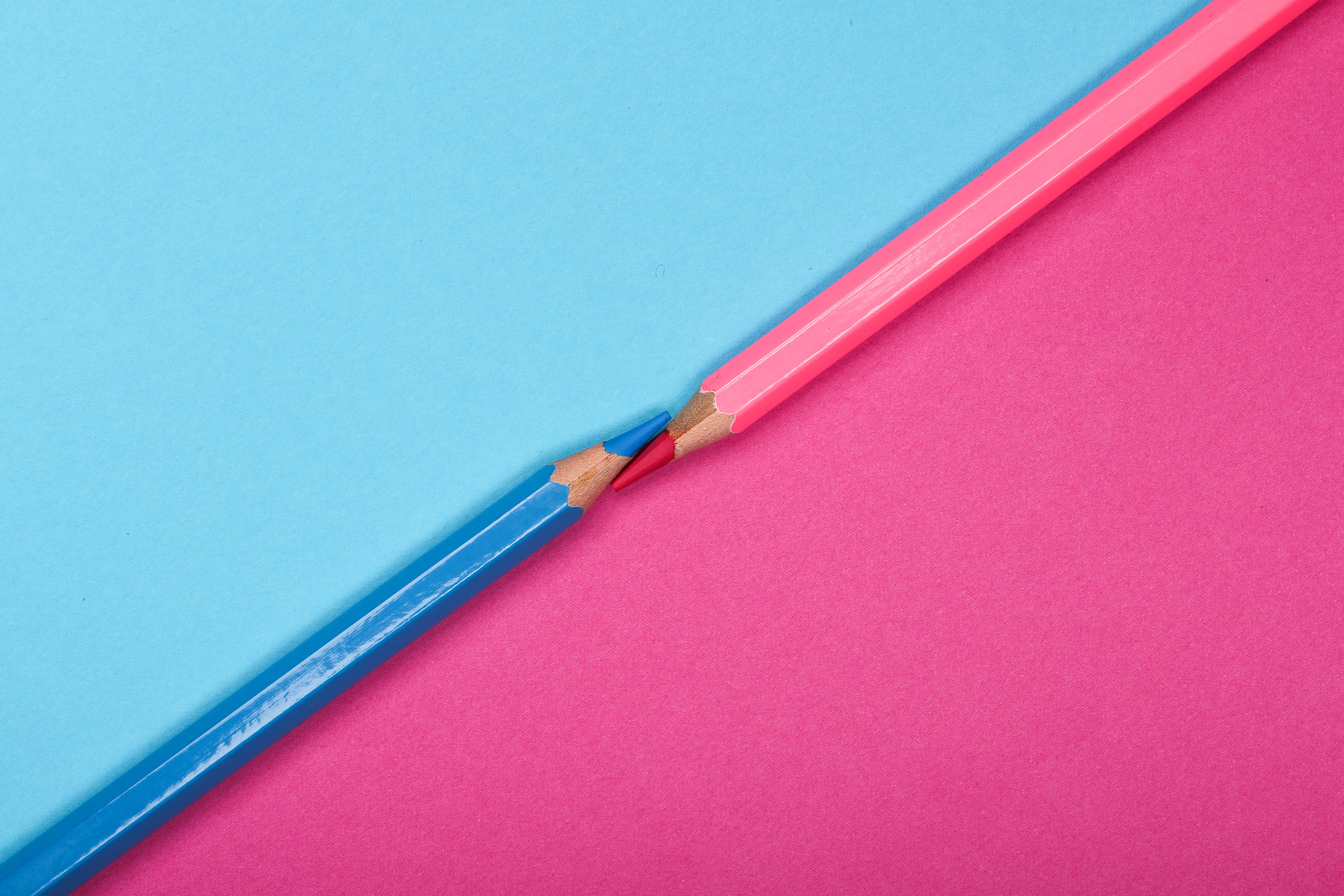 Two colored pencils meet on a contrasting pink and blue background, symbolizing harmony and creativity.
