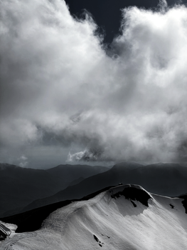 Stunning grayscale image of a snow-covered mountain ridge beneath a dramatic cloudy sky in Russia.