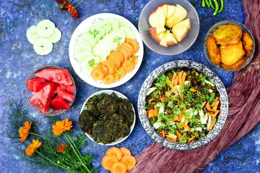 A vibrant overhead view of a colorful vegetarian meal set with salads and fruits on a textured backdrop.