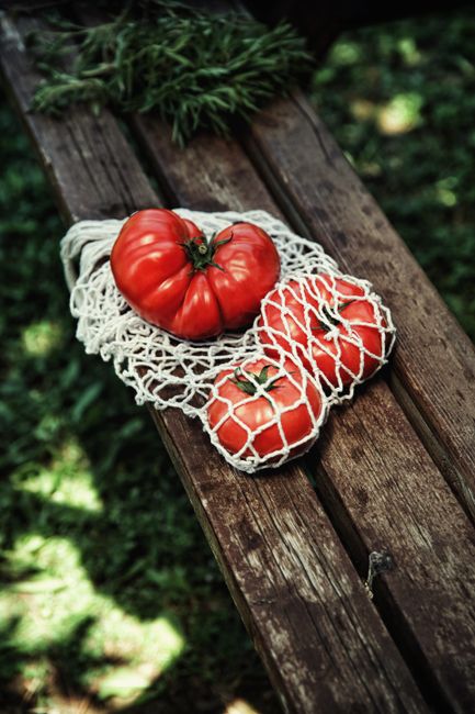 Close-up of ripe red tomatoes in a net bag on an outdoor wooden bench.