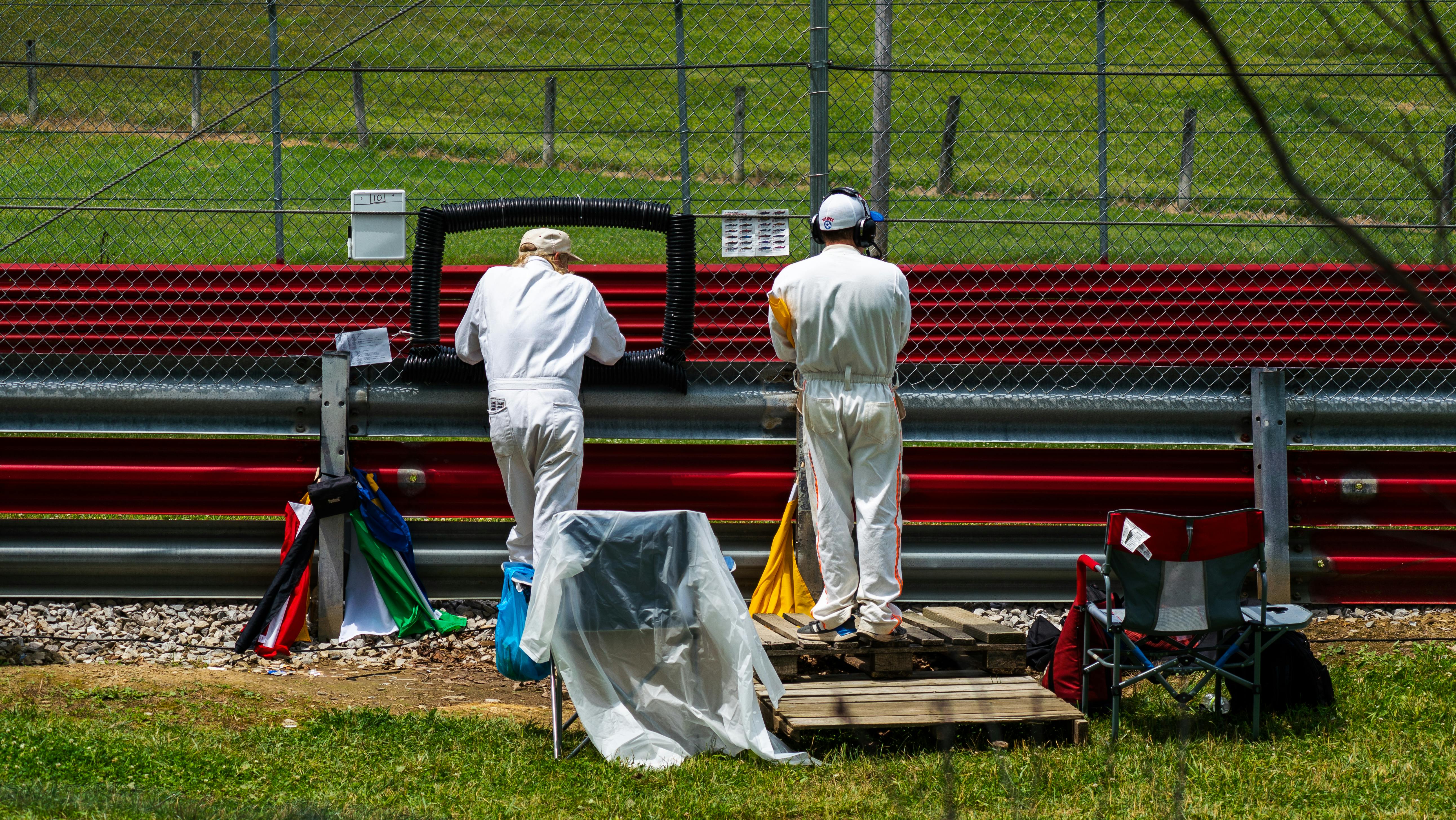 pit crews behind a chain link fence