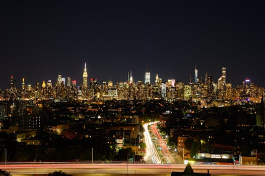 Stunning nighttime view of New York City skyline with vibrant lights and long exposure traffic trails.