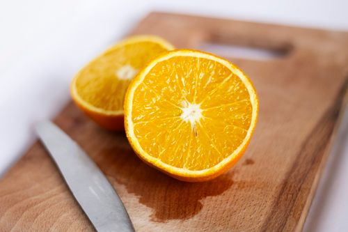 Free Close-up of a juicy sliced orange on a wooden board with a knife, capturing freshness. Stock Photo