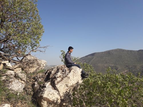 Free A man sitting calmly on a rocky ledge overlooking a scenic mountain landscape on a clear day. Stock Photo