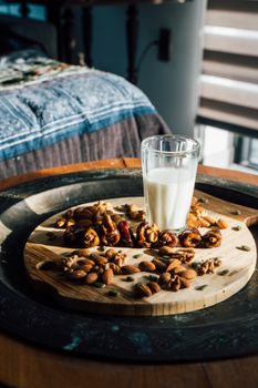 A glass of milk surrounded by a variety of nuts and dates on a cutting board, perfect for a nutritious snack.