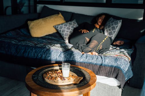 Glass of Milk, Almonds, and Date Fruits in Bedroom with a Woman Sleeping on a Couch