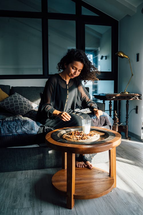 Woman in Black Dress Sitting on Sofa While Having a Breakfast 