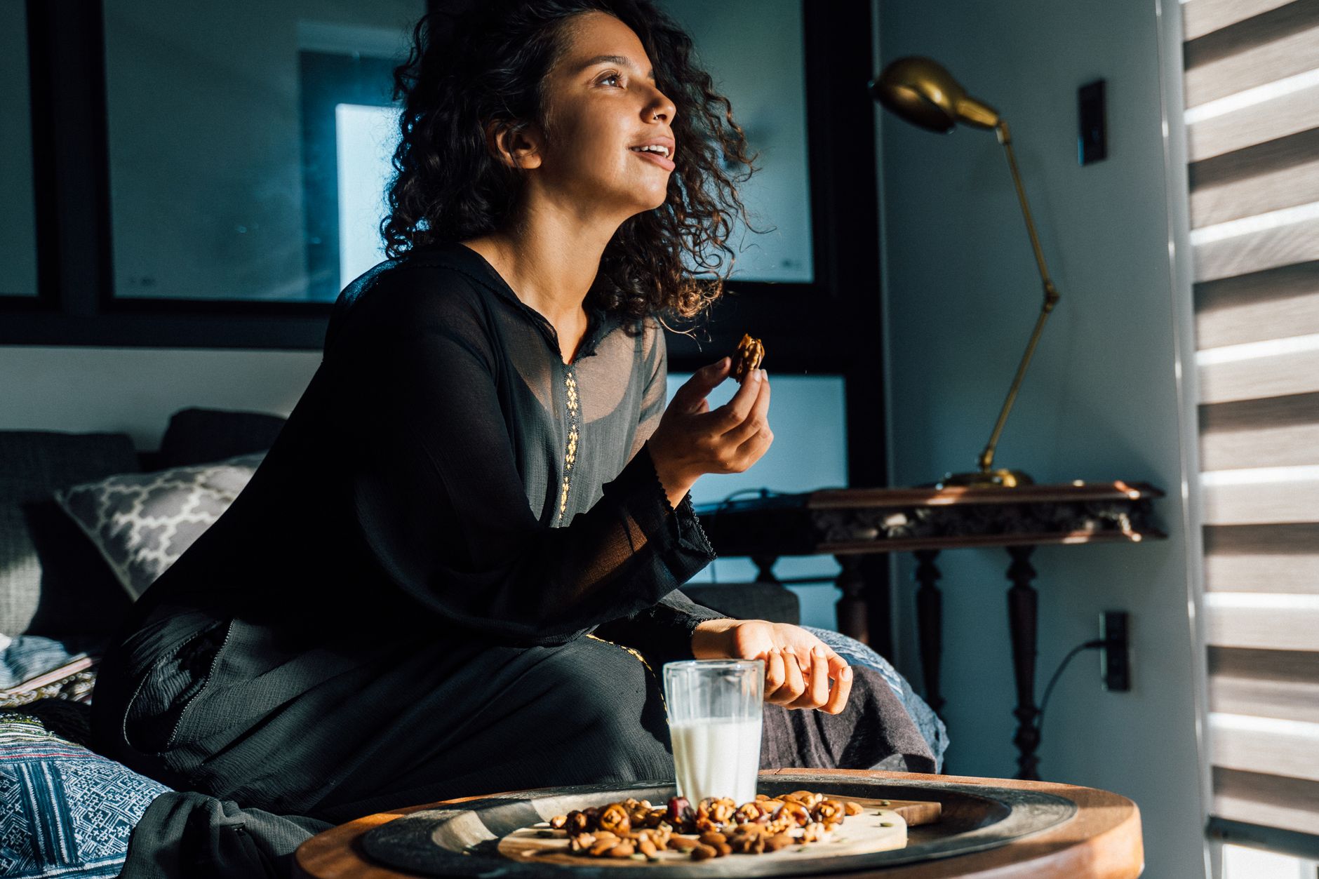 Woman in black dress enjoying walnuts and milk on a wooden board indoors.