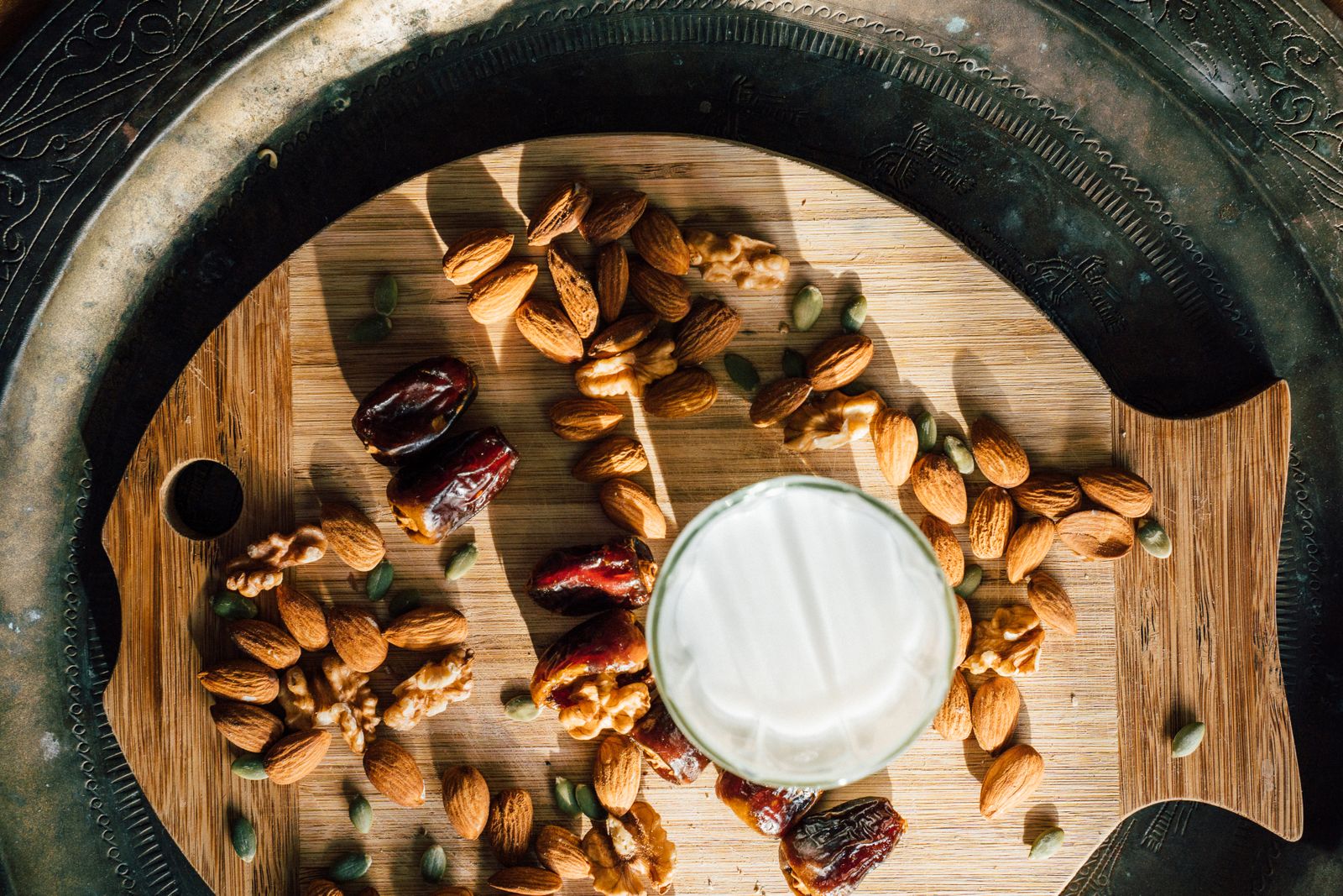 Almonds, prunes, and a glass of milk arranged on a wooden board, representing a mindful eating window after fasting