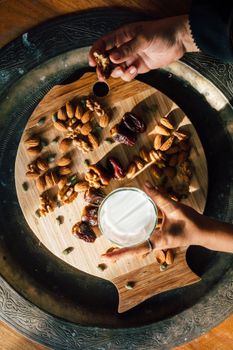 A vertical shot featuring almonds, walnuts, seeds, and a glass of milk on a decorative wooden board.