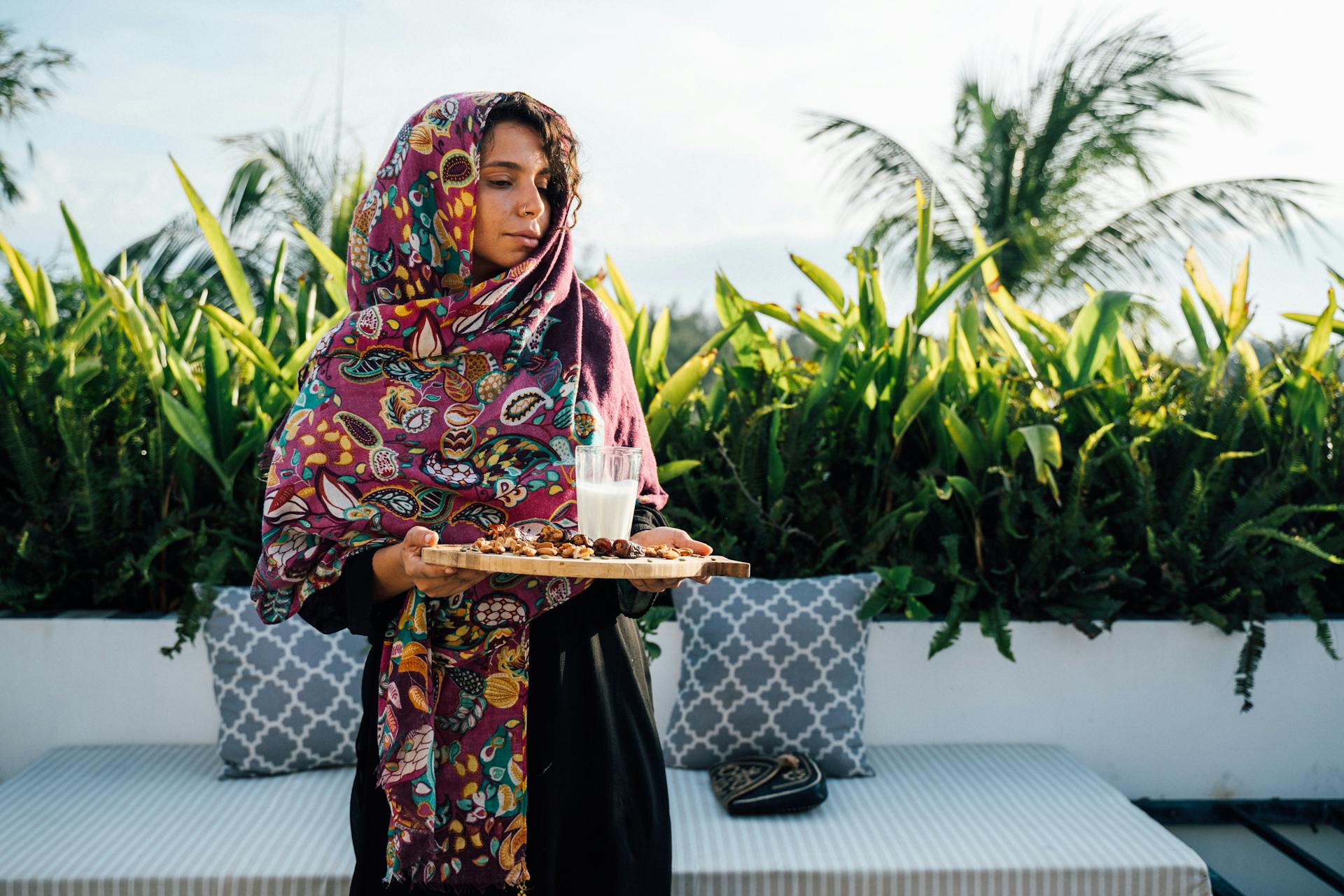 Woman in colorful shawl holding a tray with milk and dates outdoors. Perfect for Ramadan-themed collections.