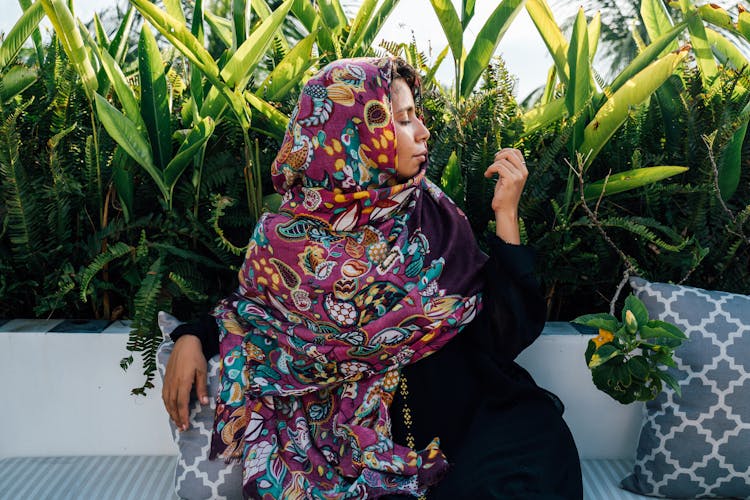 Woman In Hijab And Black Abaya Sitting On A Couch Near Plant 