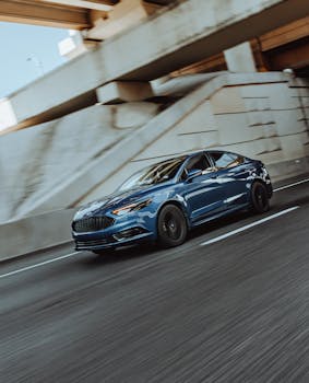Blue car speeding on a city highway under an overpass, showcasing modern design and speed.